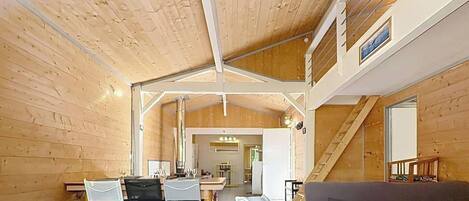 A spacious room with a high ceiling, wooden walls, a dining area with chairs and a table, and a sofa.
