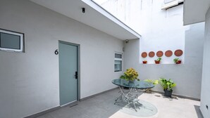 A modern outdoor patio with a glass table, potted plants, and a door marked with the number 6. - Loft a 15 min de Fundidora | Mundial 2026 (Monterrey)
