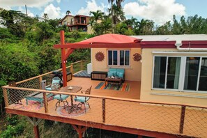 Une terrasse dotée de mobilier d’extérieur, d’un espace salon couvert et offrant une vue sur la verdure et les bâtiments environnants.