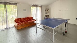 Een kamer met een tafeltennistafel, een bank en een boekenplank.