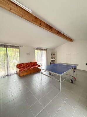 A room with a ping pong table, a sofa, and a bookshelf.