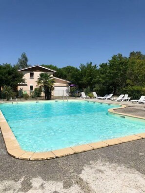 A swimming pool with lounge chairs, a building in the background, and trees around.