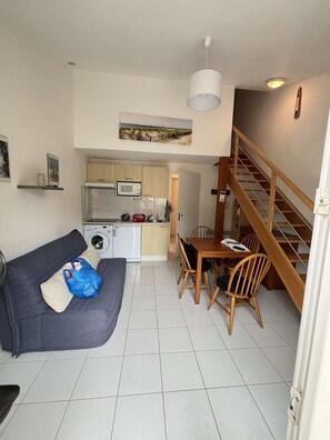 A compact living space with a kitchenette, a dining area, a sofa, and a staircase.