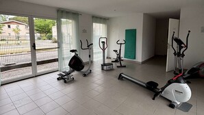 Een ruime kamer met een grote schuifglazen deur, een hometrainer, een elliptische trainer en een loopband.