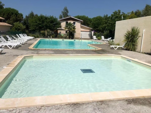 Une piscine avec des chaises longues et un bâtiment en arrière-plan.