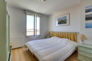 A bedroom with a bed, a window, a nightstand, a lamp, and a wall-mounted picture. - CAPBRETON with ocean view, apartment for 6 people (CAPBRETON)