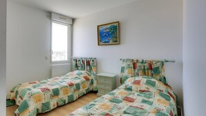 A bedroom with two beds, a window, a painting, and a ceiling light. - CAPBRETON with ocean view, apartment for 6 people (CAPBRETON)