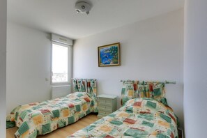 Quarto com duas camas, uma janela, um quadro e uma luminária no teto.