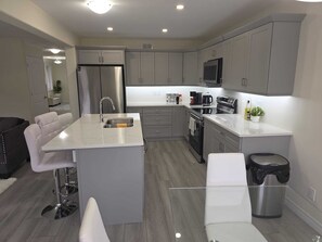 A modern kitchen with grey cabinets, stainless steel appliances, a central island with seating, and a trash bin.