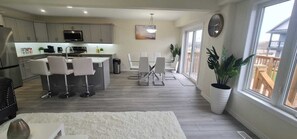 Una cocina moderna con armarios grises, una isla central con taburetes y una zona de comedor con sillas blancas, además de un ventanal con vistas.
