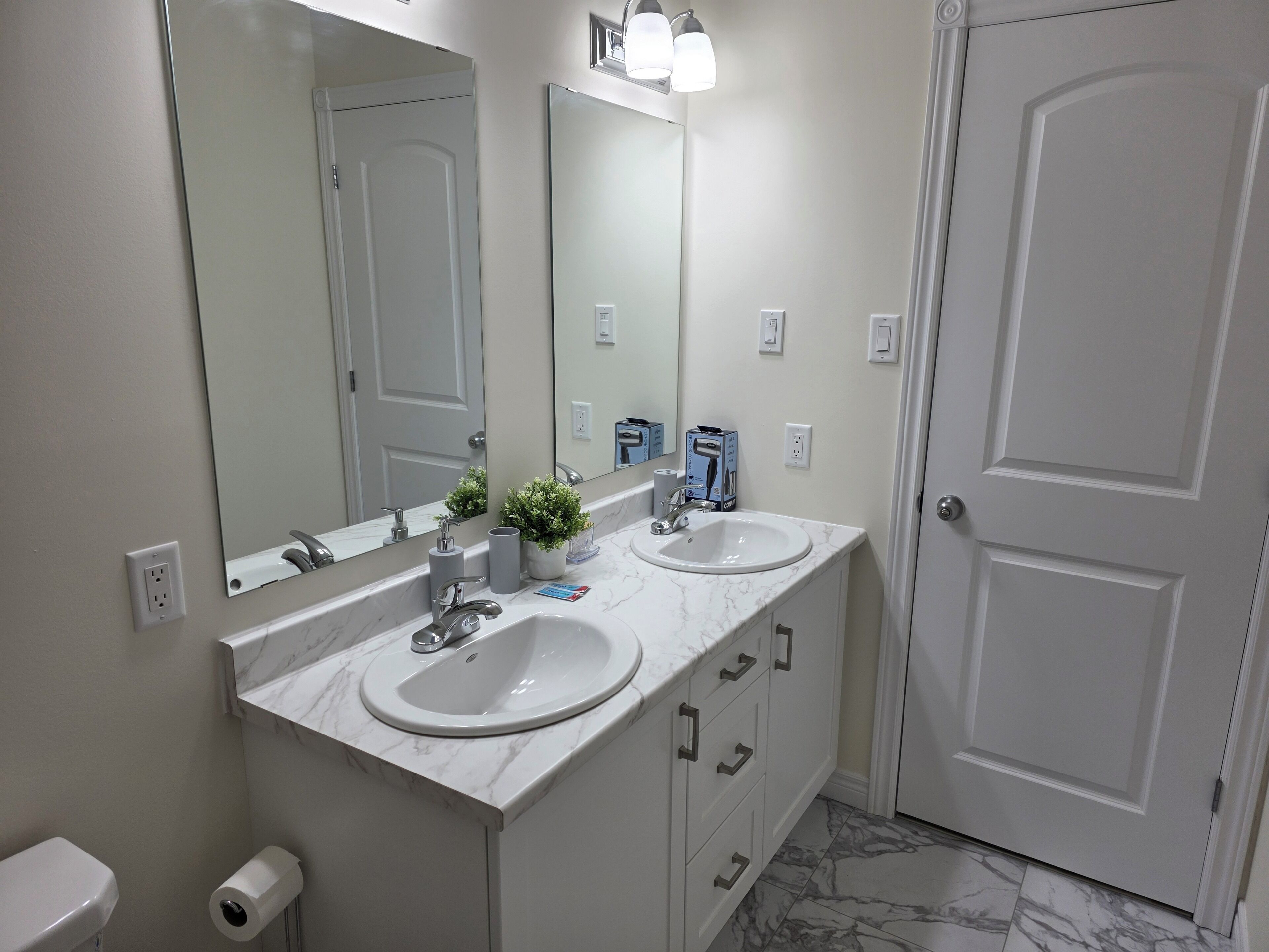 Une salle de bain avec deux lavabos, un miroir, des toilettes et une porte.