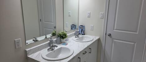 Une salle de bain avec deux lavabos, un miroir, des toilettes et une porte.