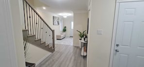 A hallway with a staircase, a white door, and a plant on a side table.
