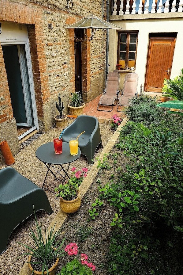 A courtyard with a seating area, a table with drinks, potted plants, and a building with a balcony. - New T2 30 m2 air-conditioned, private garden terrace, 10 mn from train station and town center. (Toulouse)