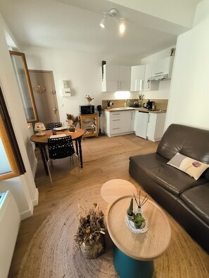 A modern living room with a brown leather sofa, a wooden coffee table, and a dining area with a wooden table and chairs. - New T2 30 m2 air-conditioned, private garden terrace, 10 mn from train station and town center. (Toulouse)