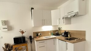 Una cocina compacta con armarios blancos, encimera de madera, microondas integrado y un lavamanos pequeño.