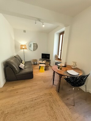 A living room with a sofa, a coffee table, a TV, and a dining area with a table and chairs. - New T2 30 m2 air-conditioned, private garden terrace, 10 mn from train station and town center. (Toulouse)