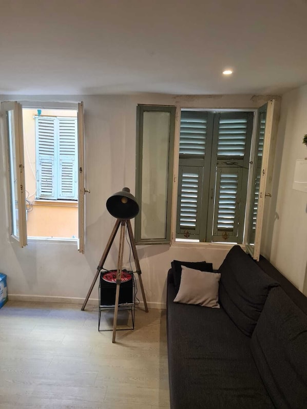 A living room with a sofa, a tripod with a camera, and a window with shutters. - Apartment in the heart of old Nice near the sea (Nice)