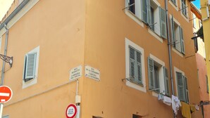 Un edificio con facciata gialla, numerose finestre con persiane, una porta nera chiusa e un cartello stradale visibile.