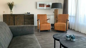 A modern living room with a grey sofa, two armchairs, a wooden cabinet, a floor lamp, and a painting on the wall. - Dijkhuis Sauna 6 (Medemblik)