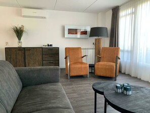 Ein modernes Wohnzimmer mit einem grauen Sofa, zwei Sesseln, einem Holzschrank, einer Stehlampe und einem Bild an der Wand.