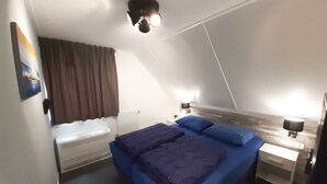 A bedroom with a bed, a heater, a nightstand with a lamp, and a ceiling light fixture. - Dijkhuis Sauna 6 (Medemblik)