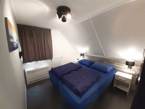 Ein Schlafzimmer mit Bett, Heizung, Nachttisch mit Lampe und Deckenleuchte.