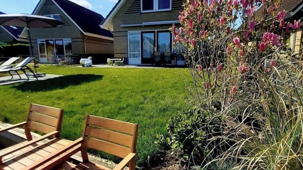 A residential property with a well-maintained lawn, a patio with wooden furniture, and a house with a gabled roof and large windows. - Dijkhuis Sauna 6 (Medemblik)