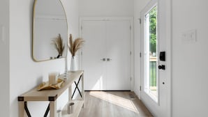 A hallway with a wooden console table, a mirror, pampas grass, and a white door. - Chic Bespoke 4BR Home: King Beds&Fully Fenced Bkyd (Clarington)