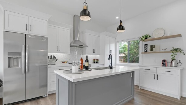 A modern kitchen with white cabinetry, a stainless steel refrigerator, a central island, pendant lighting, and a window with a view of greenery. - Chic Bespoke 4BR Home: King Beds&Fully Fenced Bkyd (Clarington)