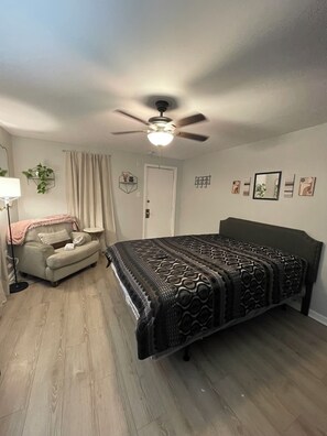 Une chambre à coucher comprenant un lit, une chaise, un ventilateur de plafond, une porte et un mur décoré.