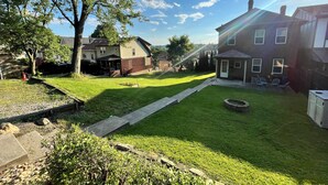 A residential backyard with a lawn, a fire pit, and a brick house. - This is the Pittsburgh View-Mt. Washington Skyline Escape! (Pittsburgh)