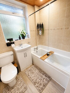 Une salle de bain comprenant des toilettes, un lavabo et une baignoire. On y trouve des articles de toilette sur une étagère, une fenêtre avec vue et un espace douche.
