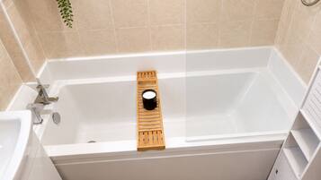 A modern bathroom with a bathtub, a wooden tray, and a small plant.