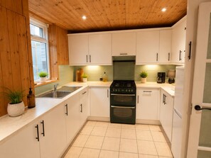 Une cuisine de taille réduite, avec des meubles blancs, une cuisinière noire et une fenêtre sur le plan de travail où sont posées des plantes.