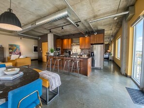 A modern kitchen with a central island, bar stools, and a dining area with a round table and chairs. - Industrial Loft · Walk to Westport · Sleeps 6 (Kansas City)