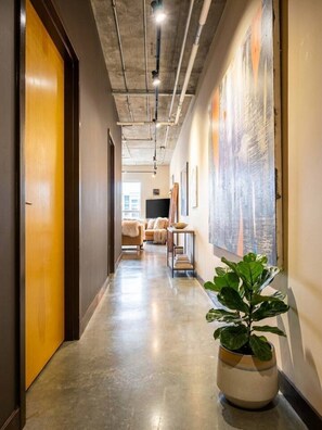 A hallway with a concrete ceiling, a potted plant, and a sofa in the background. - Industrial Loft · Walk to Westport · Sleeps 6 (Kansas City)