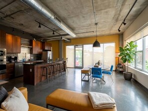 Uma cozinha moderna com um espaço bar, área de jantar com cadeiras azuis e uma janela grande que oferece iluminação natural.