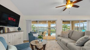 A living room with a television, sofas, a coffee table, and a view to the outside. - Peace River Retreat | Riverfront + Heated Pool (Punta Gorda)