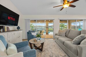 Una sala de estar con televisor, sofás, una mesa de centro y vistas al exterior.