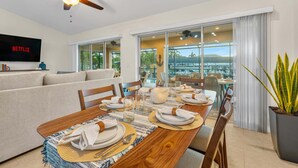 A dining area with a wooden table set for four, a ceiling fan, and a TV displaying 'NETFLIX' on the wall. - Peace River Retreat | Riverfront + Heated Pool (Punta Gorda)