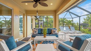 A sunroom with a ceiling fan, a sofa with blue cushions, a coffee table, and a view of the outdoors. - Peace River Retreat | Riverfront + Heated Pool (Punta Gorda)