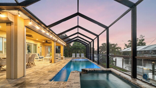 A swimming pool with a glass enclosure, lounge chairs, and a patio area with tables and chairs. - Peace River Retreat | Riverfront + Heated Pool (Punta Gorda)