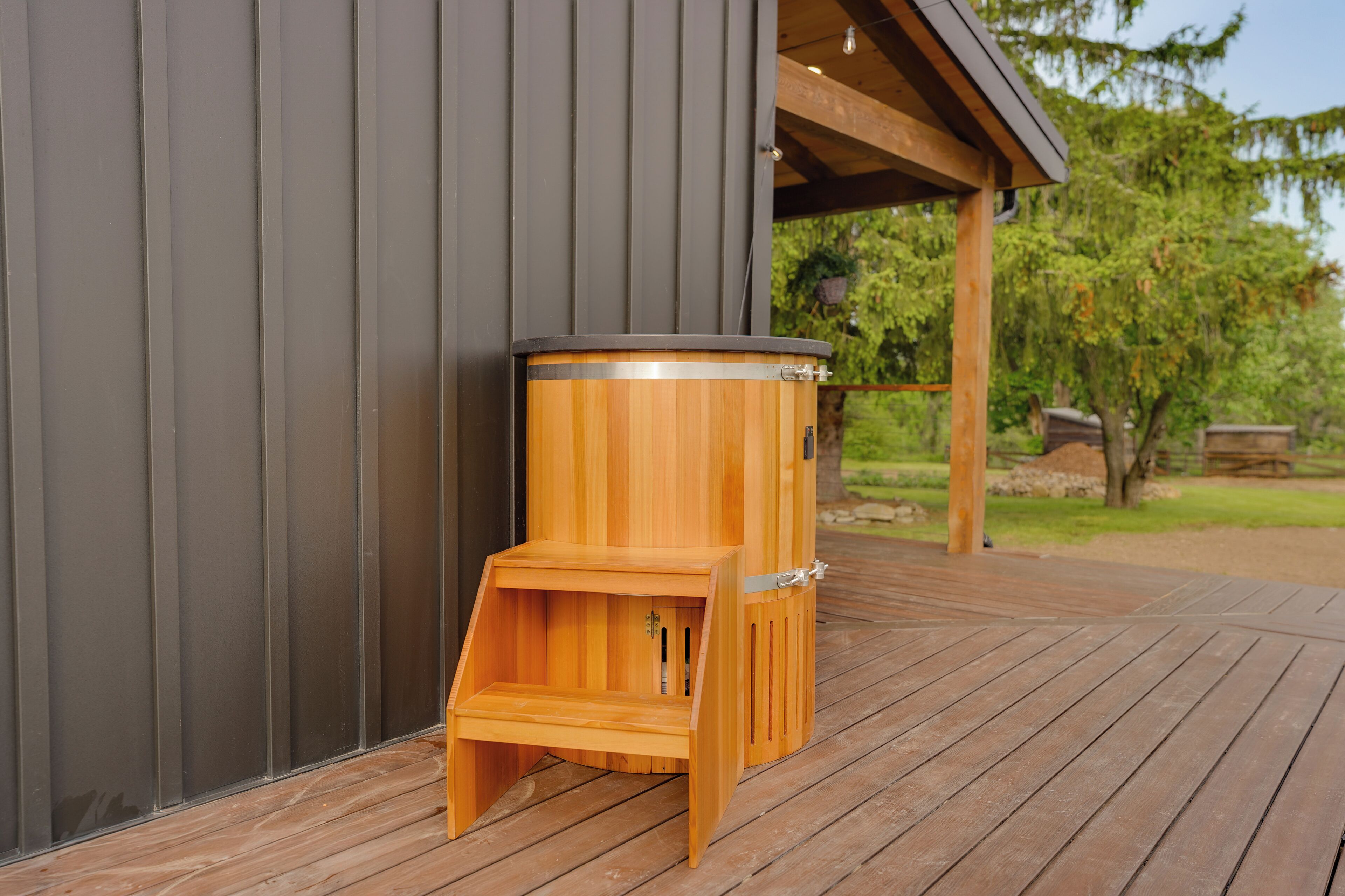 A wooden sauna structure on a wooden deck, adjacent to a metal wall.