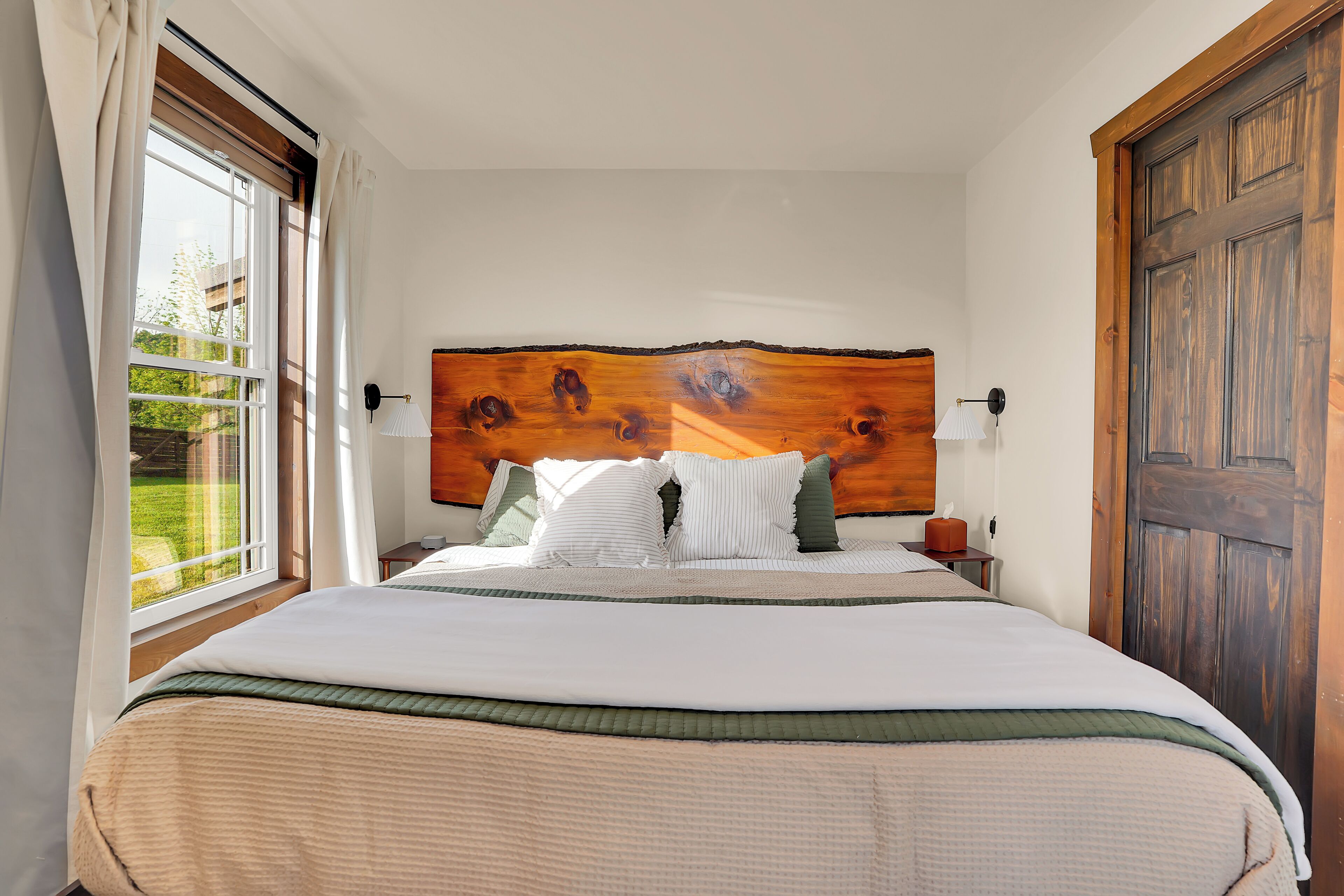 Una camera da letto con un letto grande, una testata in legno, una finestra con tende, un comodino e una porta.