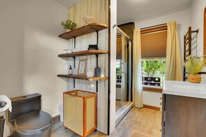 A bathroom with a toilet, a wicker basket, and shelves with toiletries.