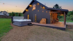 Un bâtiment moderne doté d’un jacuzzi, d’une terrasse en bois et d’un espace extérieur aménagé et abrité.