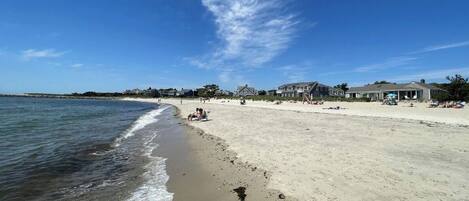 Une plage avec des maisons en arrière-plan, un ciel dégagé et une mer calme.
