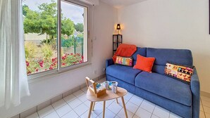Ein Zimmer mit einem blauen Sofa, einem kleinen Tisch mit Tablett, einem Fenster mit Vorhängen und einer Lampe auf einem Beistelltisch.