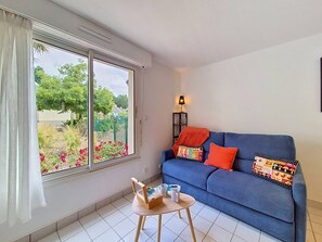 Ein Zimmer mit einem blauen Sofa, einem kleinen Tisch mit Tablett, einem Fenster mit Vorhängen und einer Lampe auf einem Beistelltisch.